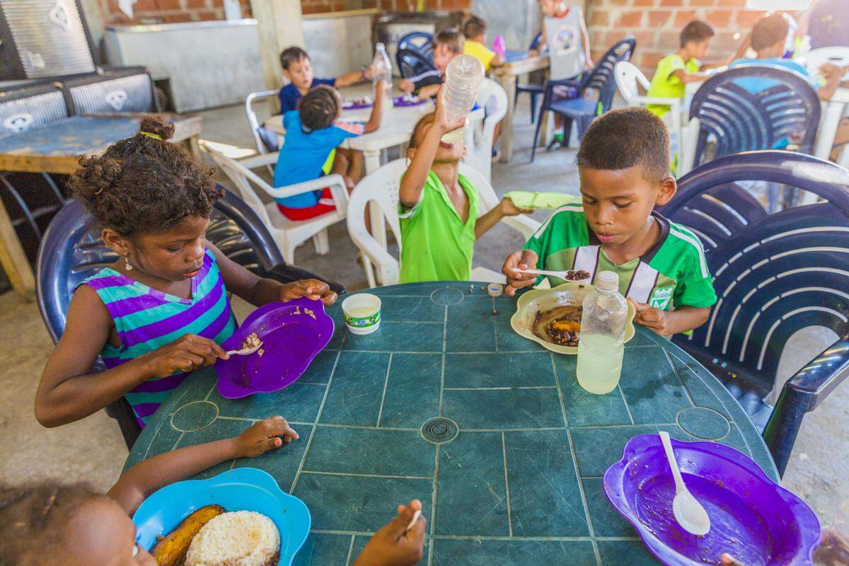 Estelita Gomez, 7, and Alexis Torres, 8, along with other children, eat food provided by the NGO Pasión Petare in Petare, Venezuela. It is often the only meal that children will receive on practice days.