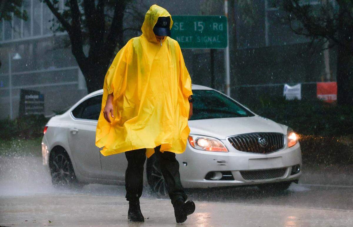 A poncho-wearing pedestrian smokes in the rain as he walks along the sidewalk off Brickell Avenue in Miami, Florida, on Tuesday, Sept. 27, 2022. This file photo was taken during a time of alert ahead of Hurricane Ian’s tropical storm-force winds. On March 29, 2023, the weather was not nearly as threatening but there were thunderstorms and reports of street flooding in parts of Miami-Dade and Broward.
