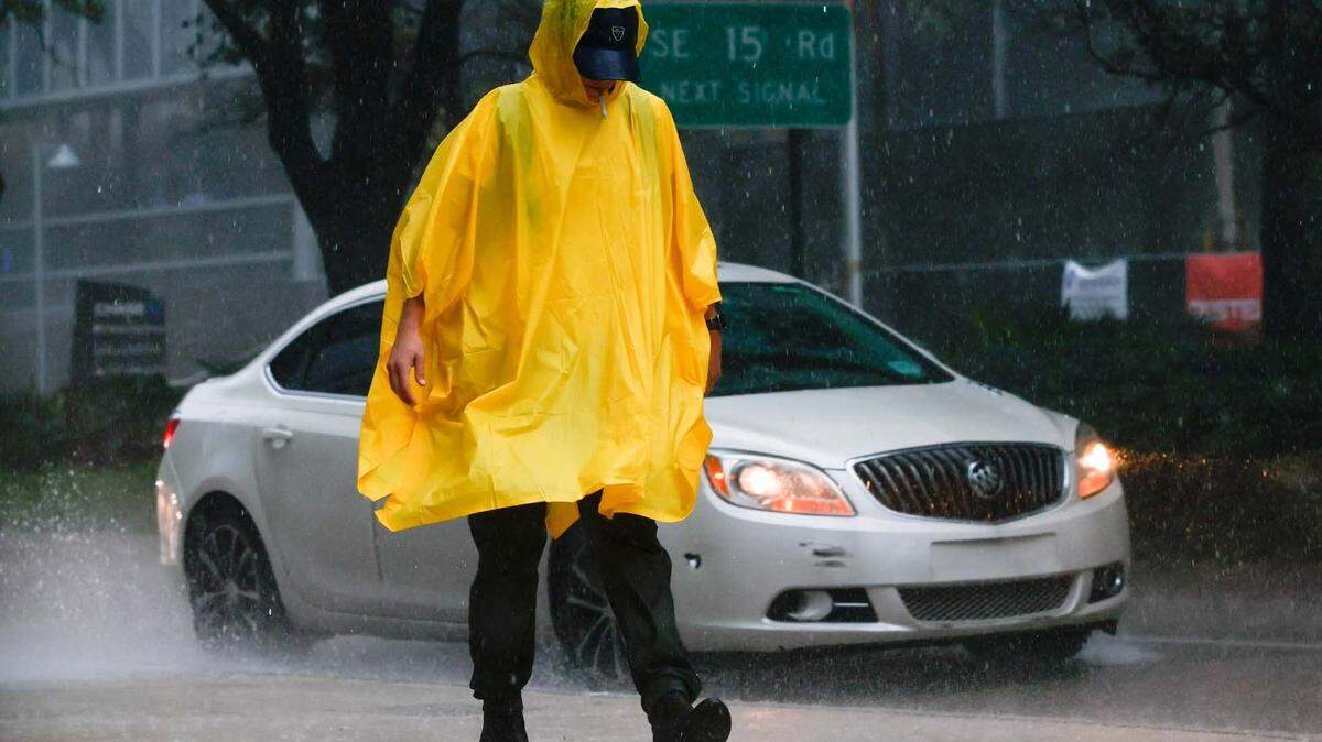 A poncho-wearing pedestrian smokes in the rain as he walks along the sidewalk off Brickell Avenue in Miami, Florida, on Tuesday, Sept. 27, 2022. This file photo was taken during a time of alert ahead of Hurricane Ian’s tropical storm-force winds. On March 29, 2023, the weather was not nearly as threatening but there were thunderstorms and reports of street flooding in parts of Miami-Dade and Broward.