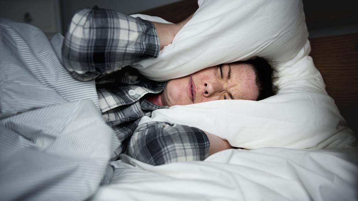 Woman holding a pillow over her ears while in bed.