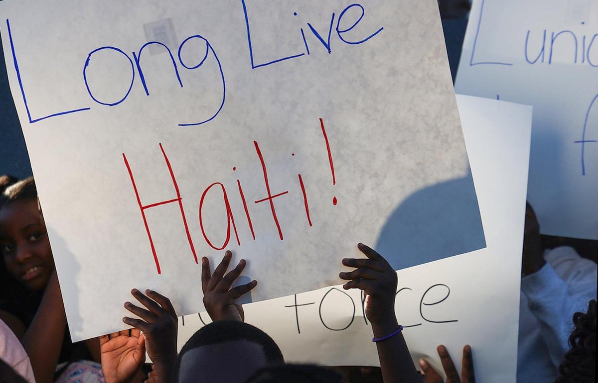 Children hold up signs in support of Haiti as members of the Haitian community and others gathered at Toussaint L’ Ouverture Statue for the customary moment of silence occurring at 4:53PM – the time of the 2010 earthquake prior to leading a procession to the Little Haiti Cultural Complex for a ceremonial remembrance of those who perished on Sunday, December 12, 2025.