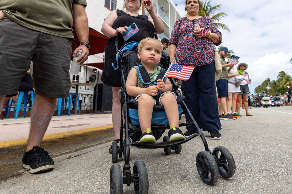 A toddler watches as parade participants drive up Ocean Drive during the 16th Annual Veterans Day Parade on Monday, Nov. 11, 2024, in Miami Beach, Fla.
