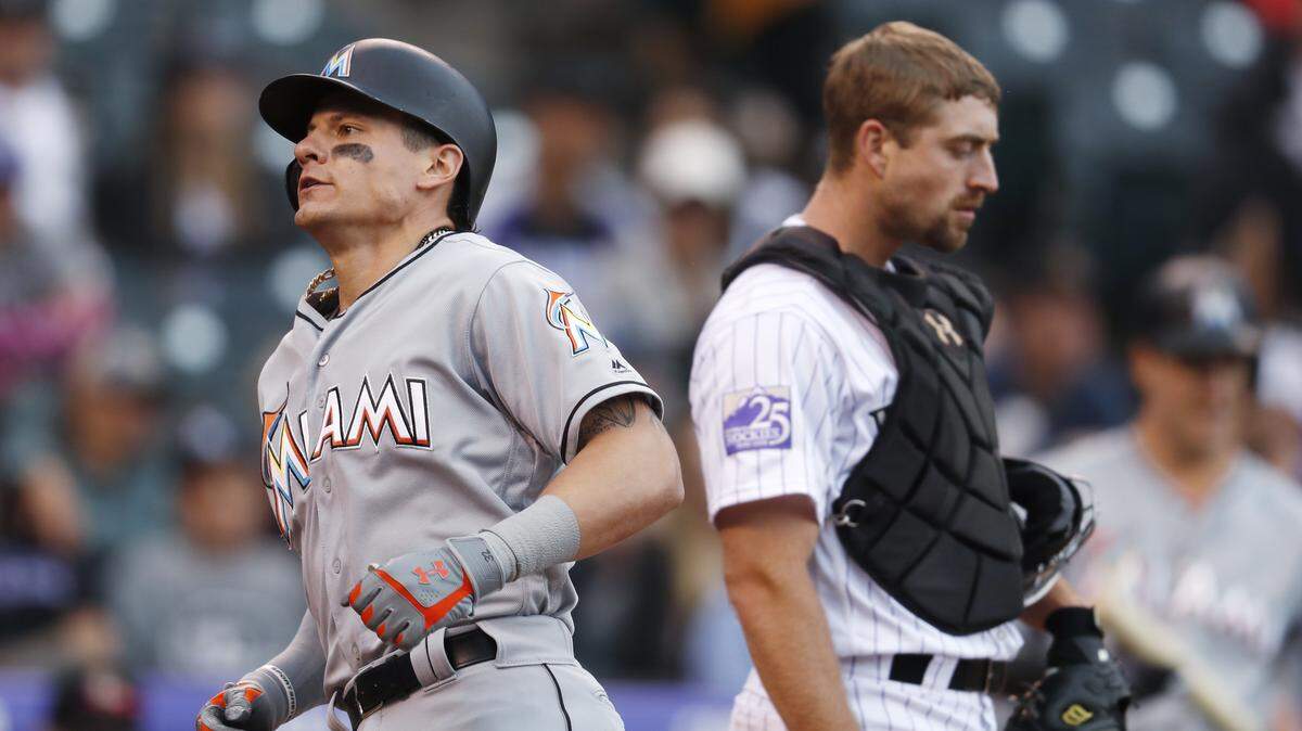 Miami Marlins' Derek Dietrich, left, crosses home plate after hitting a solo home run as Colorado Rockies catcher Tom Murphy looks on in the second inning of a baseball game Sunday, June 24, 2018, in Denver.