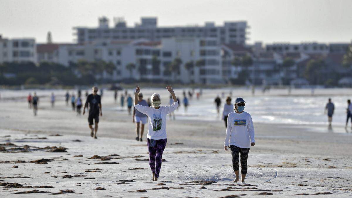 Two women wearing safety masks stretch as they walk on Siesta beach Monday, April 27, 2020, in Siesta Key, Fla. Sarasota county officials reopened beaches for essential activities, such as exercising. (AP Photo/Chris O’Meara)