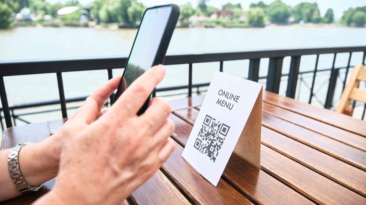 Una mujer copia un código QR con su teléfono para ver el menú de un restaurante; el uso de la tecnología sin contacto en la vida cotidiana. 