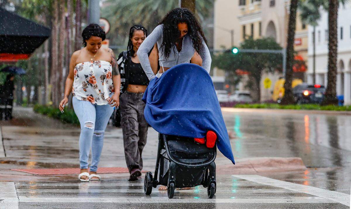 A woman pushing a baby carriage crosses the street along Ponce De Leon Boulevard in Coral Gables during a rain storm on Wednesday, November 15, 2023.