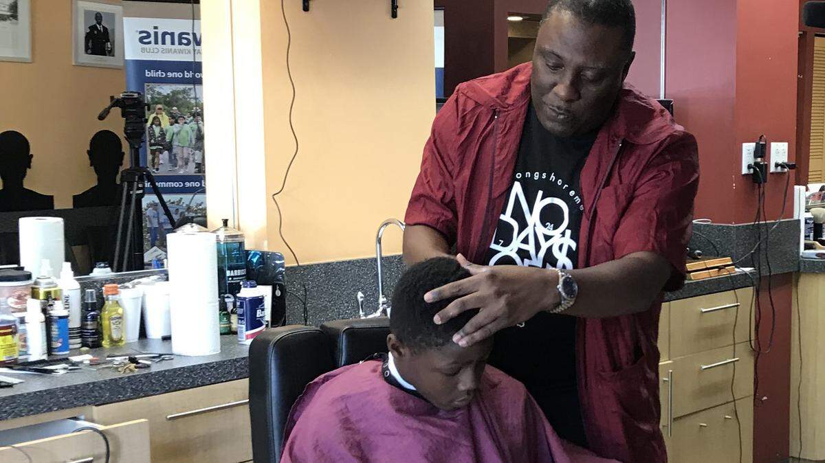 Pastor Willie Williams, owner of Just Right Christian Barbershop in Overtown, gives Lavar Patterson, 10, of Frederick Douglass Elementary School a haircut while he reads a book aloud.