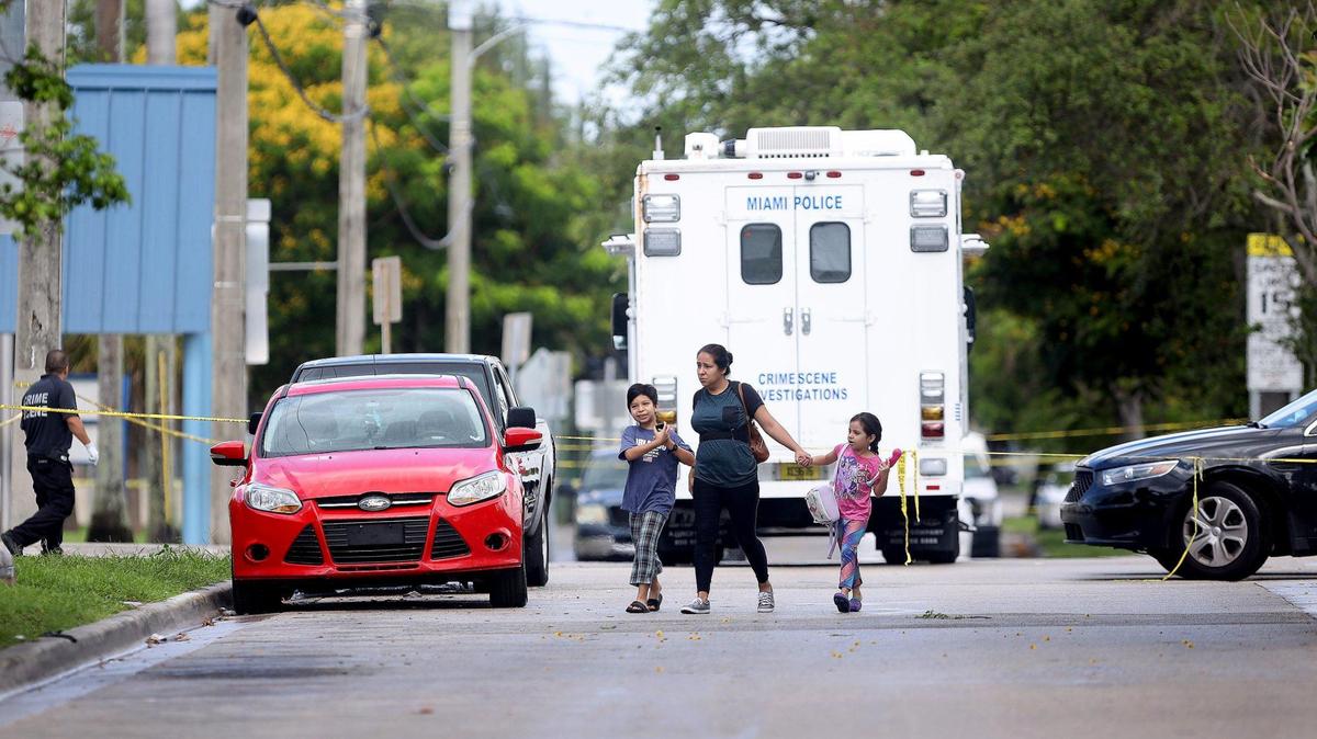 Miami Police homicide investigators work the crime scene on Wednesday, June 17, 2020 after one man was killed and another injured and transported to the hospital late Tuesday night. An unidentified mother scurry her children across the street near Toussaint Louverture Elementary at the 100 block of NE 59th Street in Little Haiti as she exits the crime scene.