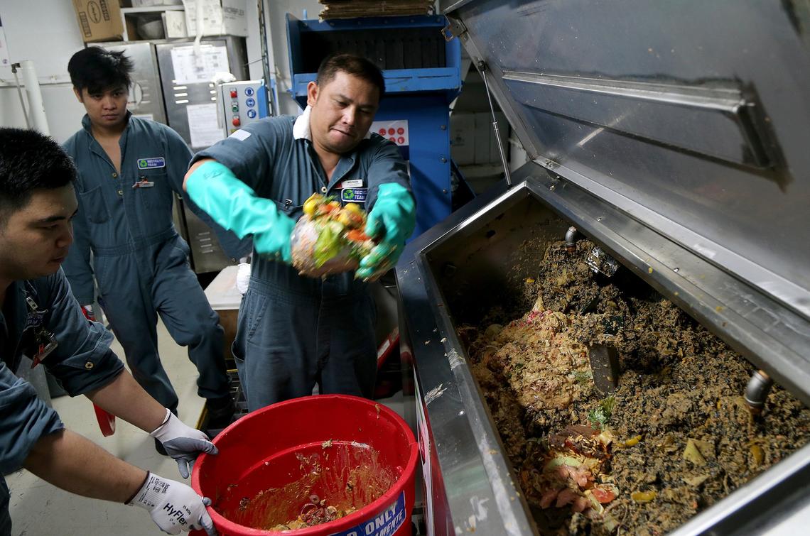 Environment team members Wilson (right) and Garry, dispose of food waste into a bio-digester, a machine that works like a human stomach to digest food waste and leave plastic behind aboard the Carnival Victory ship on Friday, October 11, 2019. Carnival Corp. is testing 20 bio-digesters across its fleet in hopes the machines will help limit the amount of plastic the company dumps in the ocean.