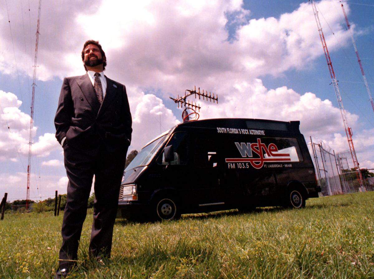 In 1995, Gary Lewis, general manager of WSHE 103.5 FM, stands in the backyard of the station with radio towers and the WSHE van in the background. The station announced itself as "South Florida's Rock Alternative," updating itself after being "She's Only Rock and Roll" for the past 25 years.