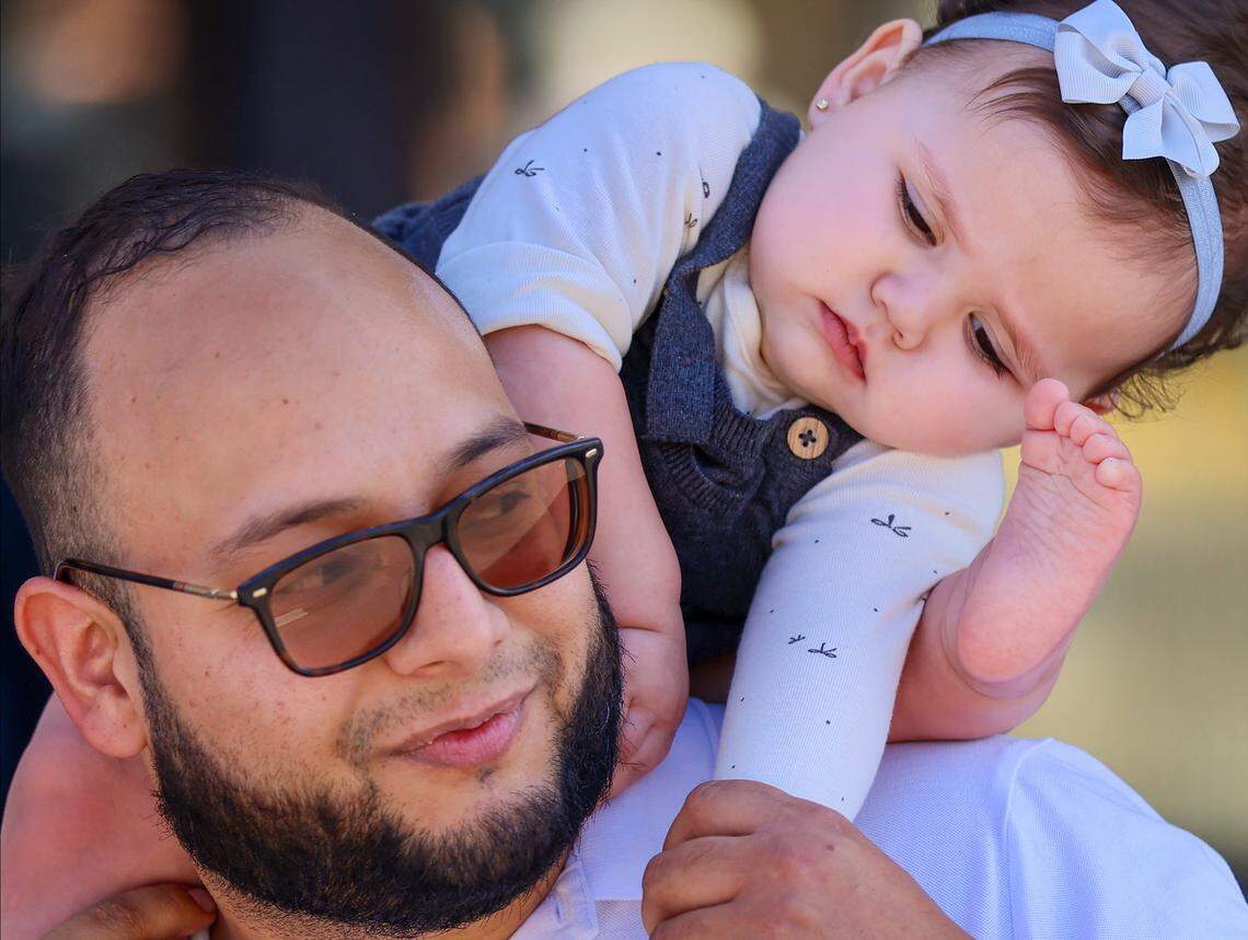 Mario Figueroa, 34, left, check on his daughter Marianna, 1, as she adjusts her posture while the pair waited for the start of the parade. 
