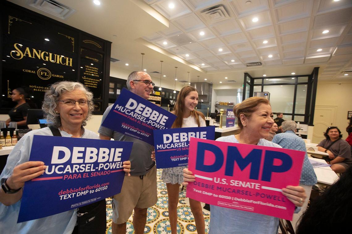 (From L to R) Lili Mucarsel, Nigel Neale, Siena Mucarsel-Powell and Sonia Neale hold signs for Senate candidate Debbie Mucarsel-Powell during a campaign event at Sanguich Coral Gables, on Sept. 22., 2024.