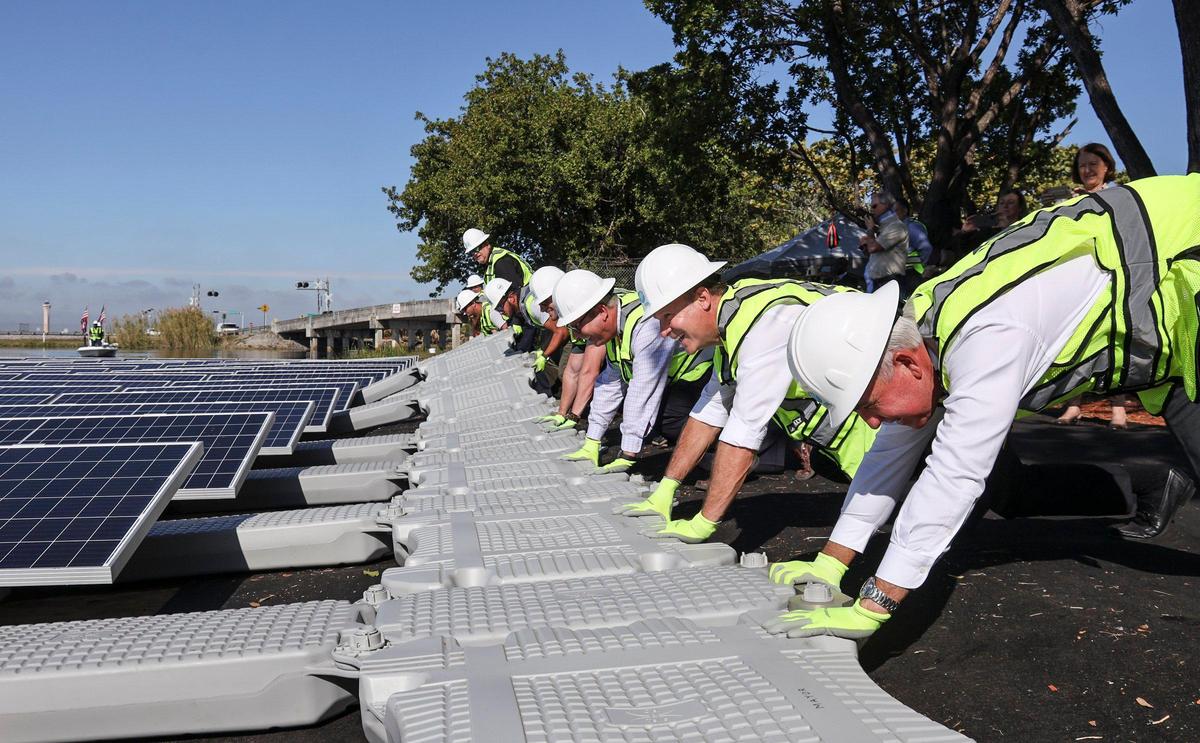 FPL CEO Eric Silagy, center, gets some help from Miami-Dade County Mayor Carlos Gimenez, right, and other company employees in launching the floating solar array into Blue Lagoon. FPL launched a half-acre, 402-panel floating solar array next to Miami International Airport on Tuesday, January 28, 2020.