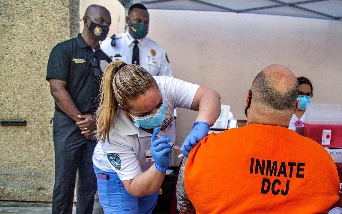 Miami-Dade County Commissioner Kionne L. McGhee (far left, rear), chairman of the Health and Emergency Management Committee, and Daniel Junior, director, Corrections and Rehabilitation — Miami-Dade County, look on as medical assistant Maria L. Rodriguez vaccinates an inmate during an event at the Miami-Dade Pre-Trial Detention Center as part of a COVID-19 vaccine program for detained residents at the Miami-Dade Corrections and Rehabilitation Department, in Miami, on March 24, 2021.
