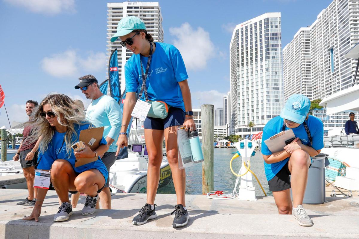Manatee observer Maranda Ealahan, center, joined by Devynne Brown, left, and Heidi Hellenbrand, right, signals after spotting a manatee that was swimming in the vicinity of the Venetian Marina & Yacht Club during the Miami International Boat Show in downtown Miami on Friday, Feb. 18, 2022.