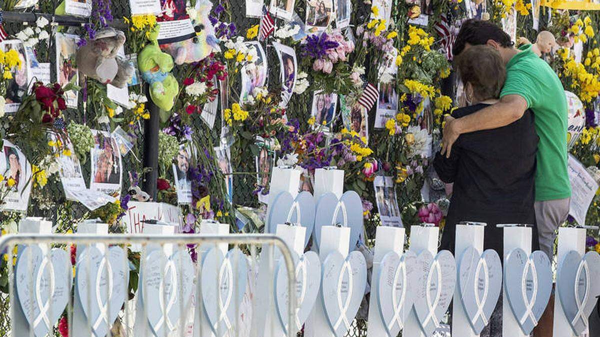 People stand at the memorial wall at the site of the deadly condo collapse in Surfside.