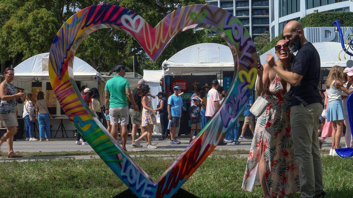 Festival attendees parade Bayshore Drive in the Grove to attend the 61st Coconut Grove Art Festival on Feb. 16, 2025. A couple of them posed by the art of Scott “Tube Dude” Gerber. Held through the Presidents' Day weekend, the festival draws tens of thousands of people to the winding streets of Coconut Grove.