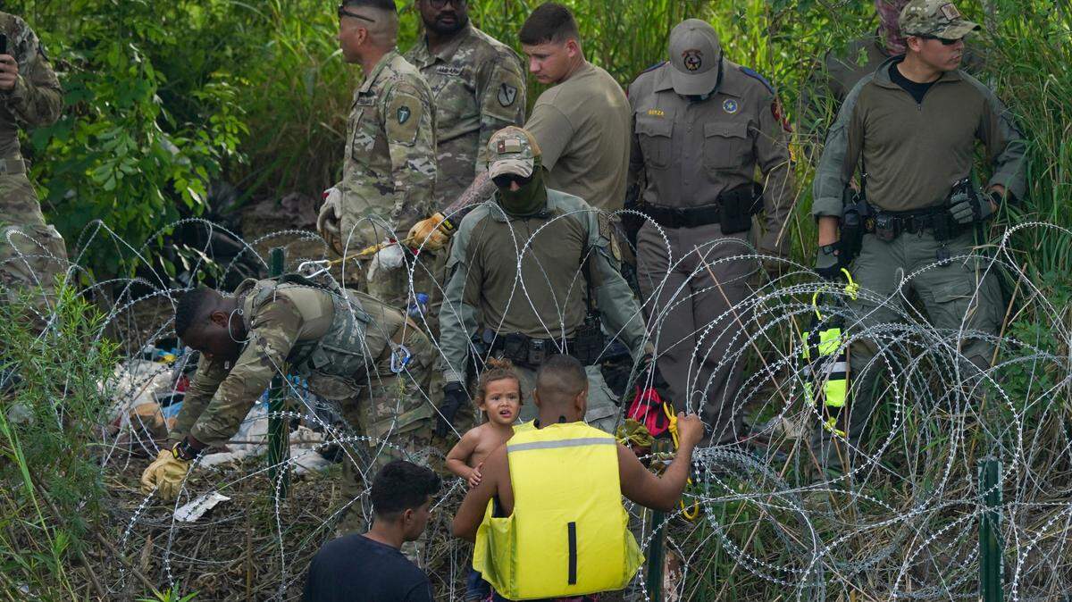Texas state police finish placing barbed wire as migrants walk up the bank of the Rio Grande, seen from Matamoros, Mexico, Wednesday, May 10, 2023. The U.S on May 11 will begin denying asylum to migrants who show up at the U.S.-Mexico border without first applying online or seeking protection in a country they passed through. (AP Photo/Fernando Llano)