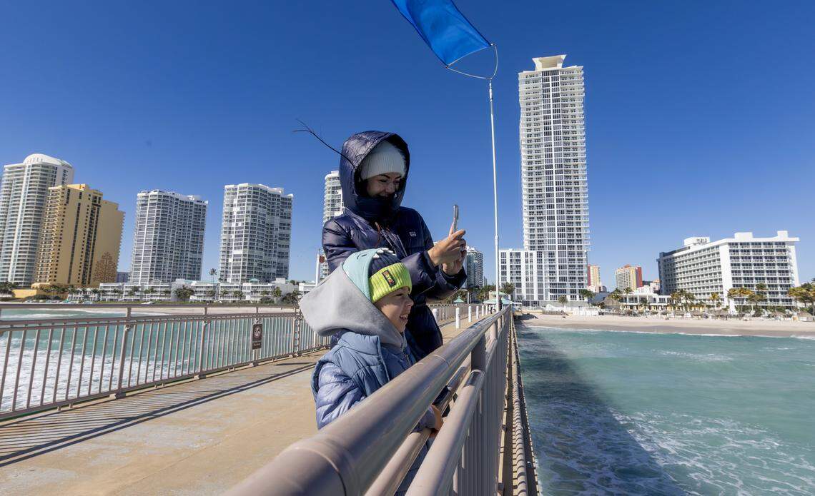 South Florida resident Anna Lysova takes photos with her son, Myron, bundled against the cold at the Newport Fishing Pier in Sunny Isles Beach, Fla., on Sunday, Feb. 1, 2026. Miami-area temperatures dipped into the 30s, the coldest in more than 15 years.