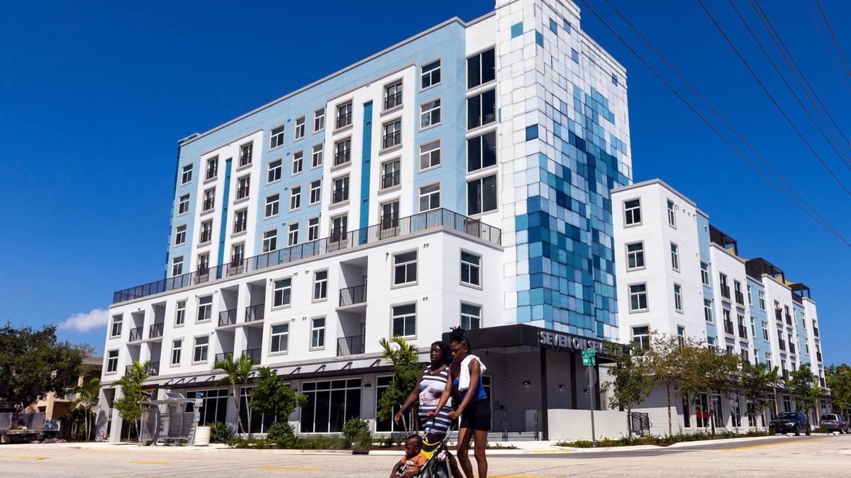 Dos mujeres con un bebé cruzan la calle frente al nuevo edificio de apartamentos Seven on Seventh, de $25 millones, en Fort Lauderdale, el 13 de septiembre de 2023. Los apartamentos son para inquilinos que necesitan viviendas estables y trabajadores locales.