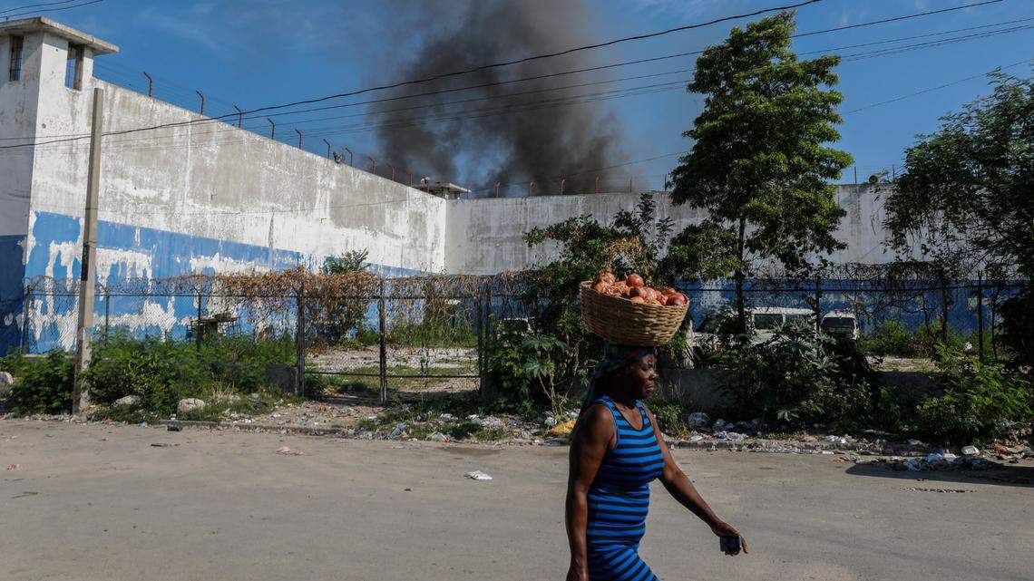 A woman walks past the smoking, empty National Penitentiary after a small fire broke out inside the jail in downtown Port-au-Prince, Haiti, Haiti, Thursday, March 14, 2024. This is the same prison that armed gangs stormed late March 2 and hundreds of inmates escaped. (AP Photo/Odelyn Joseph)