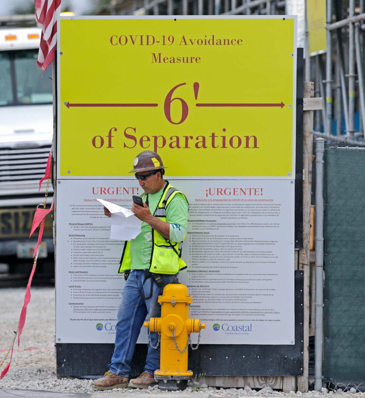 A construction worker pauses at The Estates at Acqualina construction site in Sunny Isles Beach under a sign ordering social distancing.