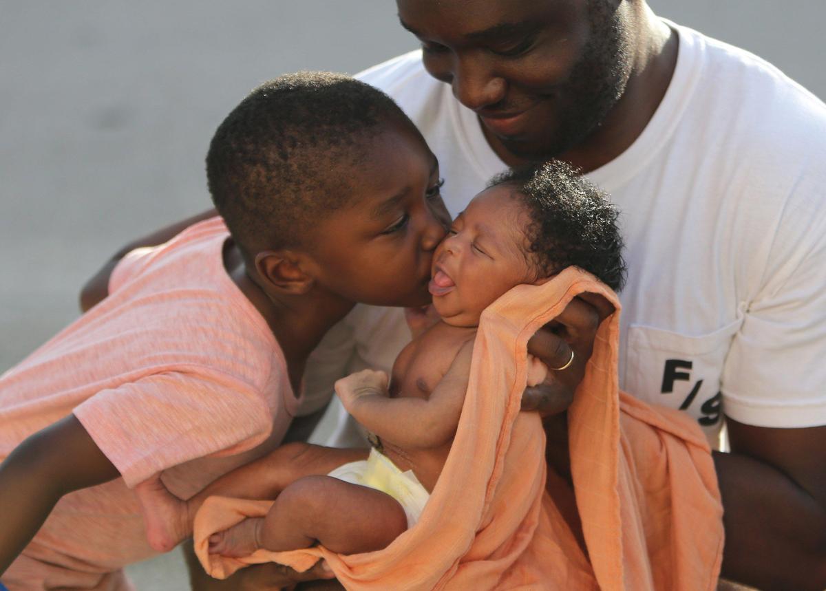Big brother, Urih Costume, 3, gives a kiss to his newborn sister, Remy, as their dad Jean holds Remy for her first outdoor outing since arriving home May 19, 2020.