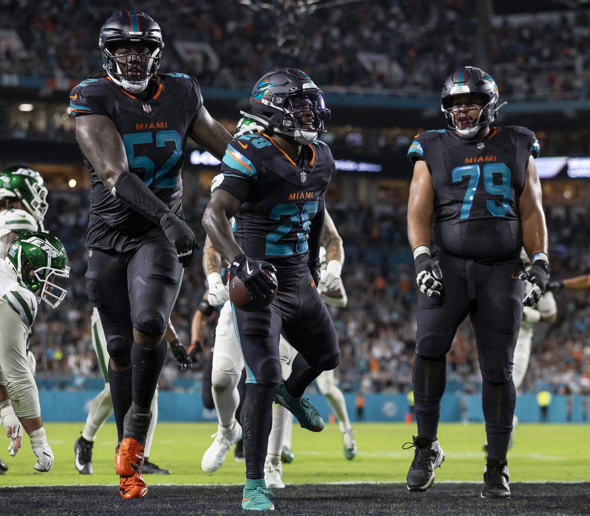 Miami Dolphins running back de'von Achane (28) celebrates with offensive tackle Patrick Paul (52) and guard Larry Borom (79) after scoring a touchdown against the New York Jets in the second half of their NFL game at Hard Rock Stadium on Monday, Sept. 29, 2025, in Miami Gardens, Fla.