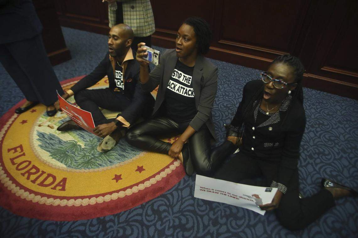 Rep. Tray McCurdy, D-Orlando, Rep. Angie Nixon, D-Jacksonville, and Rep. Felicia Robinson, D-Miami Gardens, sit on the Florida Seal in protest as debate stops on Senate Bill 2-C: Establishing the Congressional Districts of the State in the House of Representatives Thursday, April 21, 2022 at the Capitol in Tallahassee, Fla. The session was halted by the protest, but resumed an hour later.