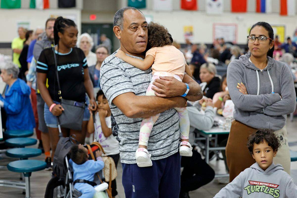 Evacuees Rolando Gallardo holds Mia Gallardo, 2, as they wait in line for lunch at the hurricane shelter in Brookside Middle School in Sarasota, Florida on Wednesday, October 9, 2024.