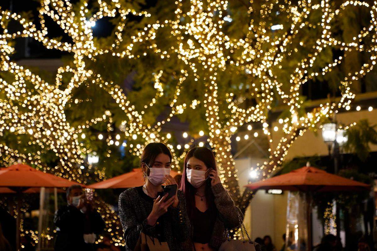Varias personas usan máscaras debajo de un árbol decorado para la temporada navideña en medio de la pandemia de COVID-19 en un distrito comercial, el miércoles 22 de diciembre de 2021 en Los Ángeles.