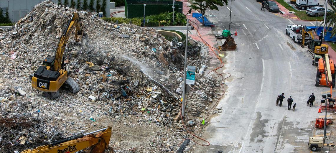 A backhoe digs through rubble on the side of Champlain Towers South that was imploded as rescue teams leave the area after their shift in Surfside, Florida, on July 13, 2021.