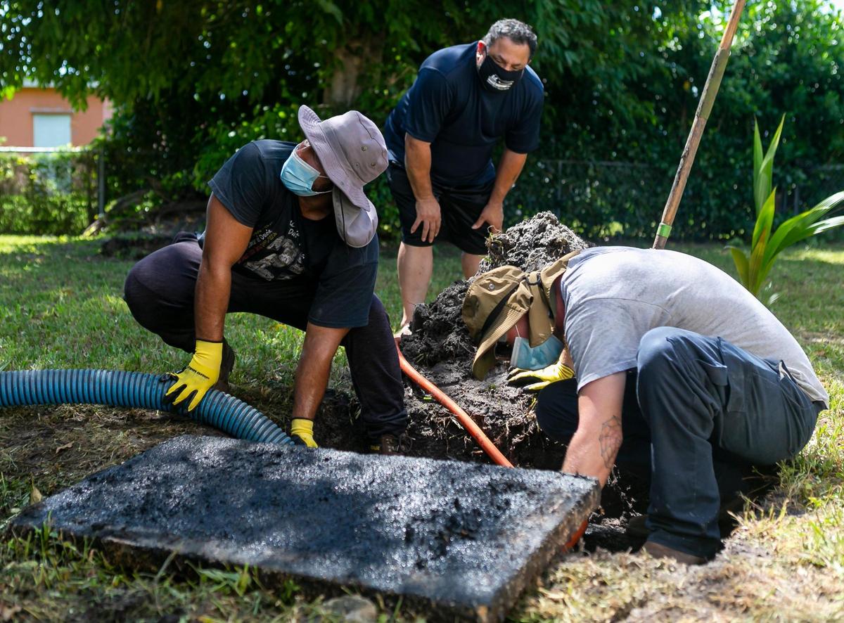 Gabriel Antivero, left, and Jeremy Langford, employees at AA ARON Super Rooter, clean out a septic tank as home owner, Ray Alvarez, watches in Miami, Florida on Wednesday, September 30, 2020.