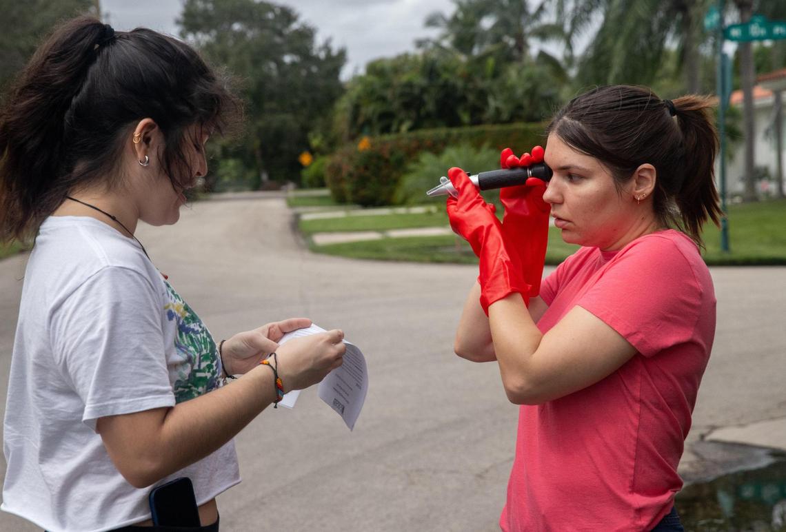Miami, Florida, October 19, 2024 - Lucero Omana, 23, left, and Mariam Medina, 26, use a refractometer device to check how salty the floodwater on a street in Miami Shores is, as part of a citizen science event for Florida International University’s Sea Level Solutions day.