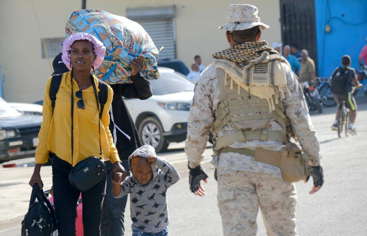 Una madre y su hijo caminan junto a un oficial de seguridad de República Dominicana en un puente fronterizo entre Dajabón, República Dominicana, y Haití, el jueves 14 de septiembre de 2023. El presidente de la República Dominicana anunció el jueves que cerrará todas las fronteras con el vecino Haití a partir del viernes en respuesta a la construcción de un supuesto canal en suelo haitiano que tiene como objetivo las aguas del río Massacre, que corre a lo largo de la frontera que comparten ambos países.