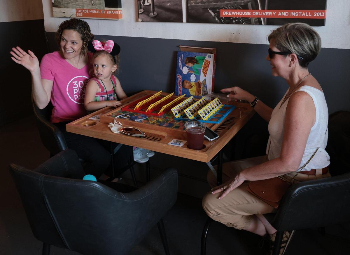 Rosemary Carrera, left, sits with her daughter, Alessi Carrera, 3, and mother, Mayra Gonzalez, right, greeting supporters with a glass of “La Rosa” during her fundraiser at Wynwood Brewing Company. The 305 Pink Pack founder held the fundraiser to raise money to provide a variety of services for those battling cancer in Miami-Dade County.