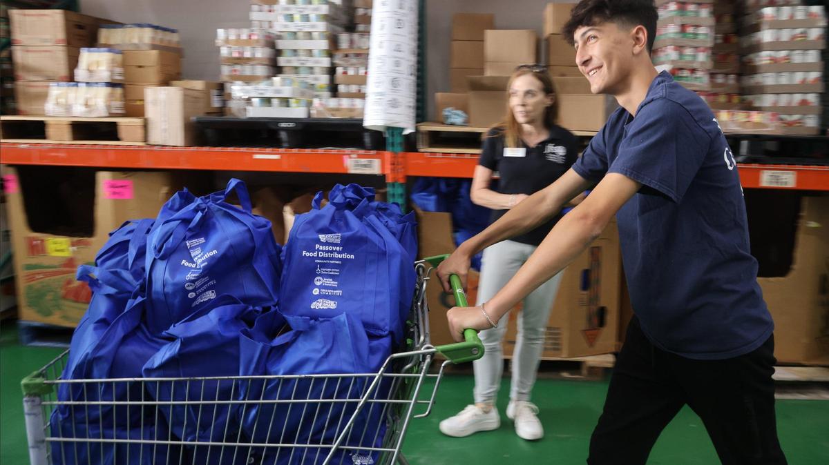 David Maratchi, 15, right, rushes past volunteers coordinator Michelle Pines, center, to deliver meal packages for transport at the Dorit & Ben J. Genet Cupboard. Broward high school volunteers sorted, stocked, and packed kosher food items as part of a Passover food distribution event to feed Broward County’s most vulnerable.