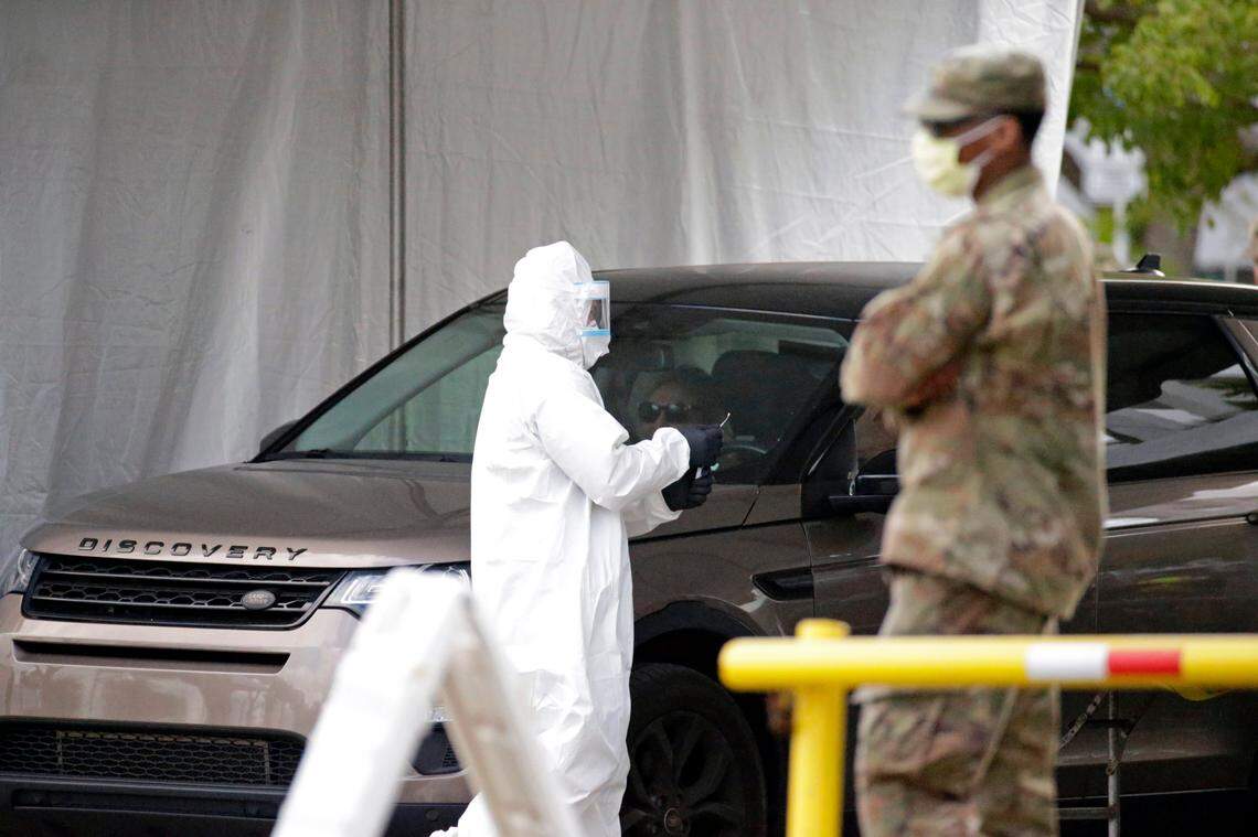 A member of the Florida Army National Guard looks on as a healthcare worker holds a swab test from a citizen at the COVID-19 drive-thru testing center at Marlins Park in Miami on Wednesday, March 25, 2020.