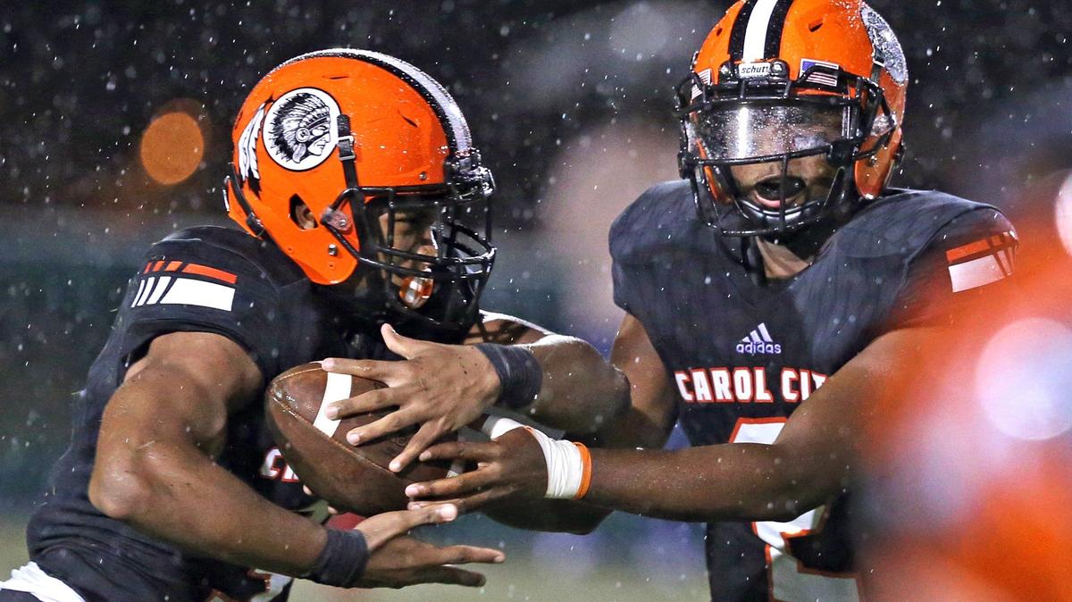 Carol City High’s quarterback Daniel Richardson hands-off to Katravis Geter (3) in the first quarter during a rain storm as Columbus plays against Carol City in football at Traz Powell Stadium on Friday, September 7, 2018.