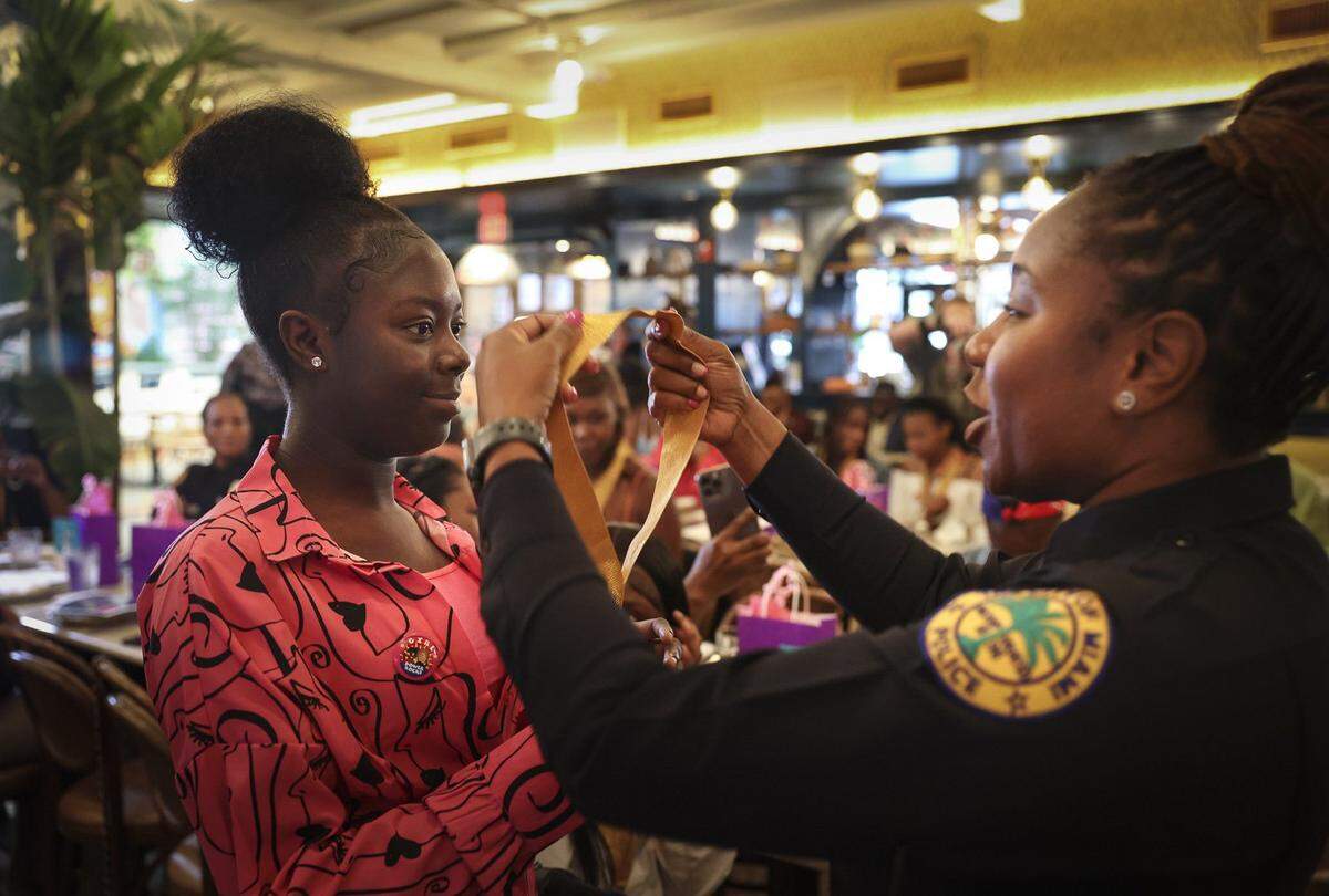 Chardonnay Johnson, left, accepts a medal from Miami police officer Tequilla Whitehead, ‘Officer Q,’ during the Teen Talk etiquette luncheon Thursday, May 18, 2023, at Red Rooster in Overtown.