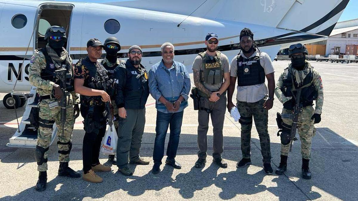 Jean Eliobert Jasme, in handcuffs, stands in the middle of this photo with DEA and Haitian National Police officers in Port-au-Prince Thursday before his transfer to the United States on new cocaine smuggling charges.