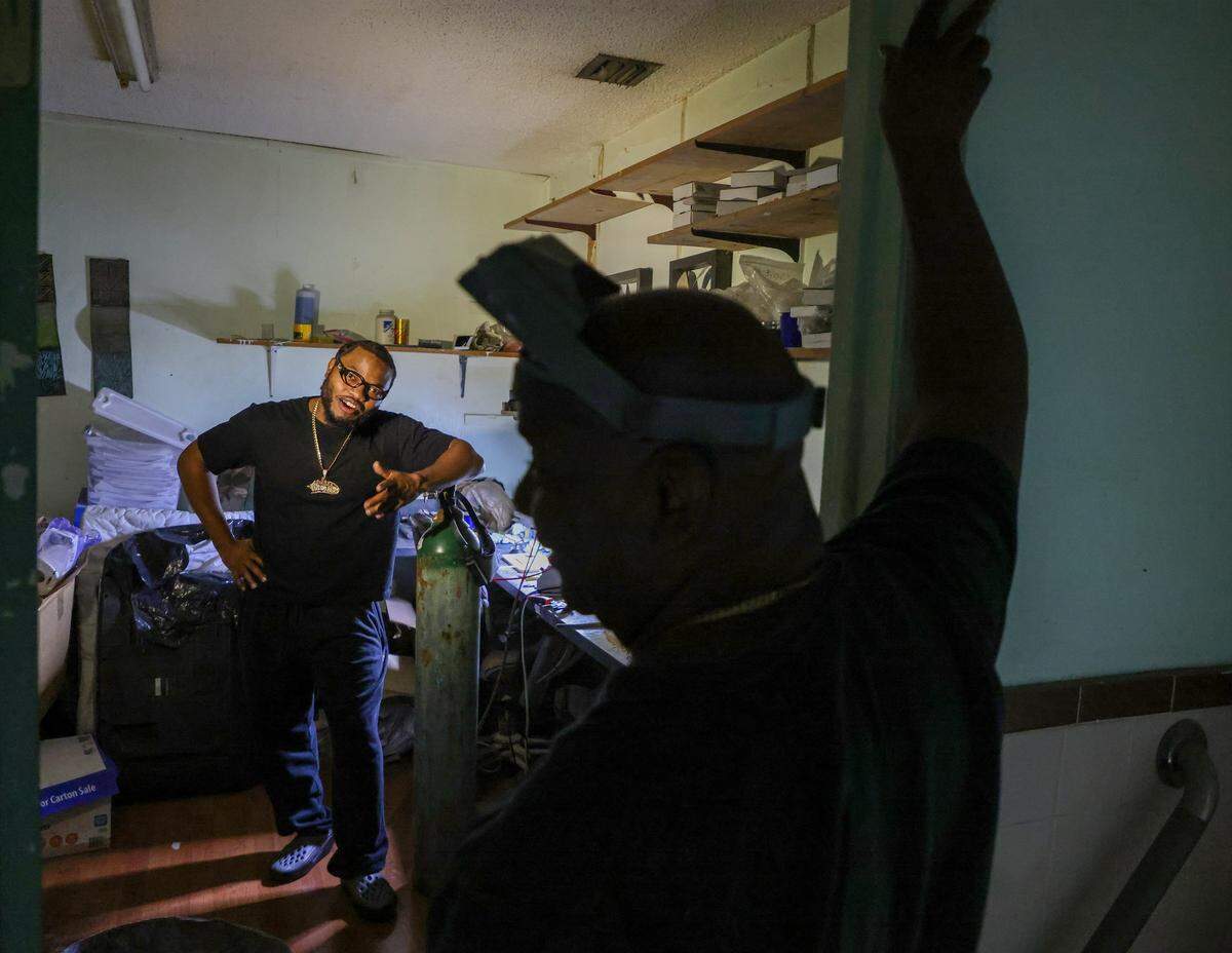 Phillip “Philo” Norville, left, is learning the business from his father, Lando Plein, right, who creates custom gold teeth and grillz at his shop, Lando Golds. 
