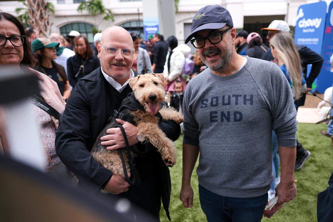 Bruce Williams, left, carries a Welsh terrier named Piper while playing a game of spin-the-wheel with Lazaro Montano, right, during the grand opening of the Chewy Bark Park at 4579 Ponce de Leon Blvd. in Coral Gables, Fla., Saturday, Jan. 31, 2026.