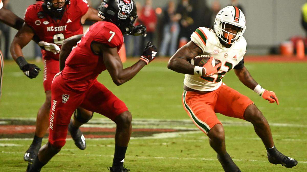 Nov 4, 2023; Raleigh, North Carolina, USA; Miami Hurricanes running back Mark Fletcher Jr. (22) runs as North Carolina State Wolfpack cornerback Shyheim Battle (7) defends during the first half at Carter-Finley Stadium. Mandatory Credit: Rob Kinnan-USA TODAY Sports
