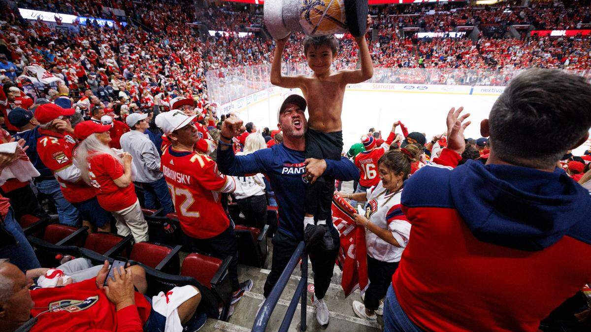 Florida Panthers fan Alex James and his dad hoist their Stanley Cup in celebration of a goal by Florida Panthers center Evan Rodrigues (17) during the second period of Game 5 of the NHL Stanley Cup Final at the Amerant Bank Arena on Tuesday, June 18, 2024 in Sunrise, Fla.