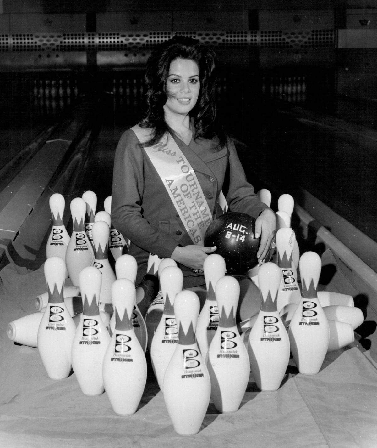 Jossie Lynn Martinez of Miami, 1971 Miss Tournament of the Americas, looks out from a “forest” of pins while inviting bowlers to the ninth annual Tournament of the Americas at Cloverleaf Lanes in North Miami-Dade.
