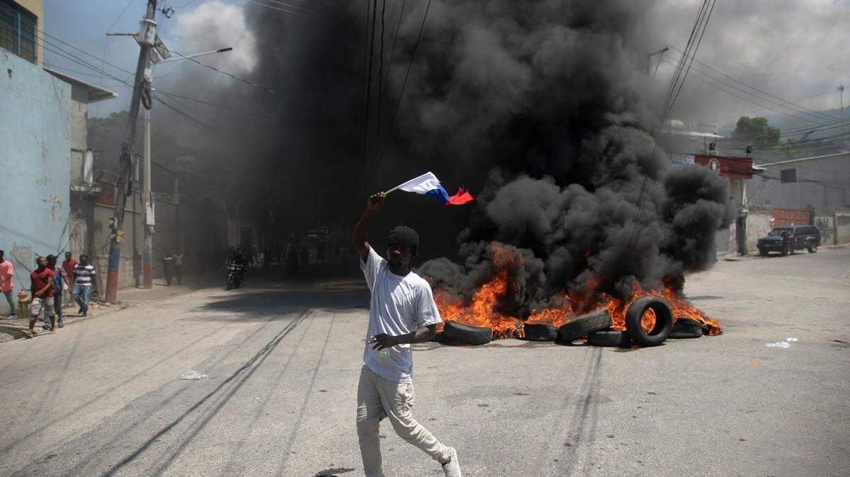 A man waving a Russian national flag walks past a burning barricade in Port-au-Prince, Haiti, during a protest to demand the ouster of Prime Minister Ariel Henry on Wednesday, Sept. 7, 2022.
