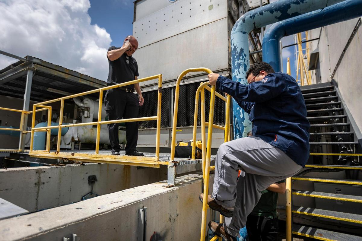 Dr. Ibrahim Ahmed, right, climbs down from where the building chillers are installed on the roof of 550 Biltmore Way after installing sensors on the power lines to collect data.