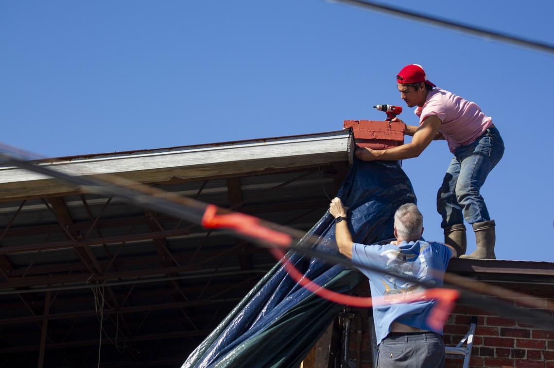 Rick Taylor, bottom, and his nephew, Marcel Duarte, work to patch their warehouse with a blue tarp in Port Saint Joe, Florida, eight days after Hurricane Michael devastated the area, leaving hundreds of thousands without shelter, power and food.