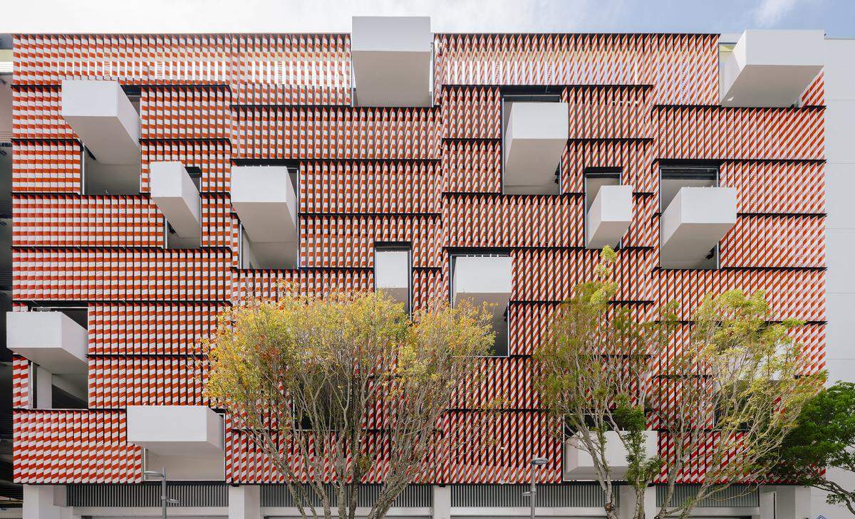 The Museum Garage’s “Barricades” facade, by architect Terence Riley, consists of a screen of orange- and white-striped metal traffic barricades punctuated by protruding concrete planters.